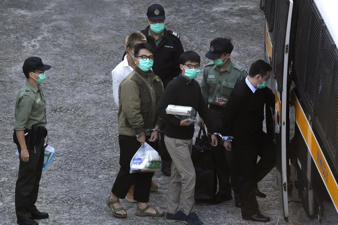 Hong Kong activists Joshua Wong, right, and Ivan Lam, left, are escorted by Correctional Services officers for a prison van before appearing in a court on Dec. 2, 2020. (AP)