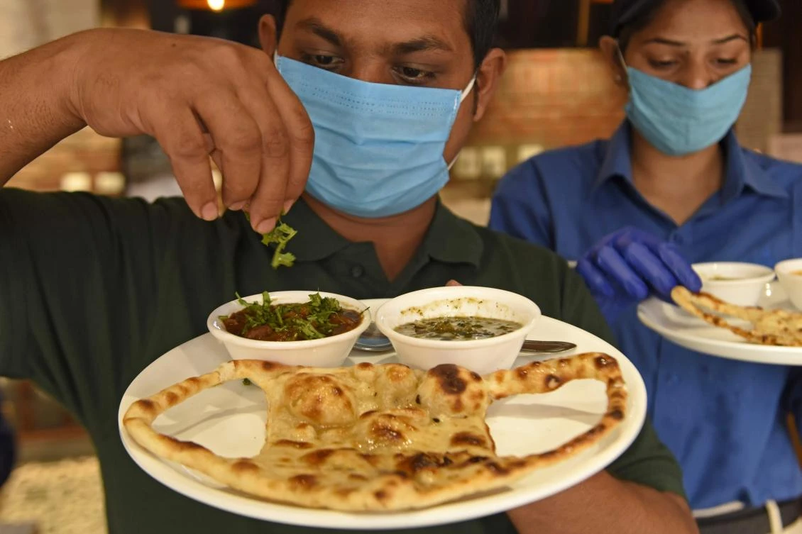 A staff member garnishes a dish with bread themed in a facemask design as part of an awareness for Covid-19 coronavirus, before serving to the guests at a food court in Amritsar on December 4, 2020. (AFP)