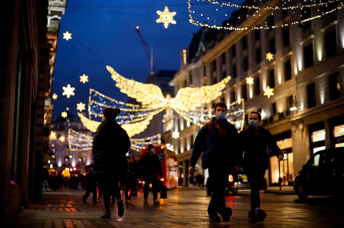 Pedestrians and shoppers, some wearing a face mask or covering due to the COVID-19 pandemic, walks beneath Christmas lights in London on December 19, 2020. (AFP)