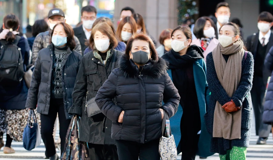 People wearing face masks to help curb the spread of the coronavirus walk across a traffic intersection in Ginza shopping district in Tokyo, Tuesday, Dec. 22, 2020. (AP)