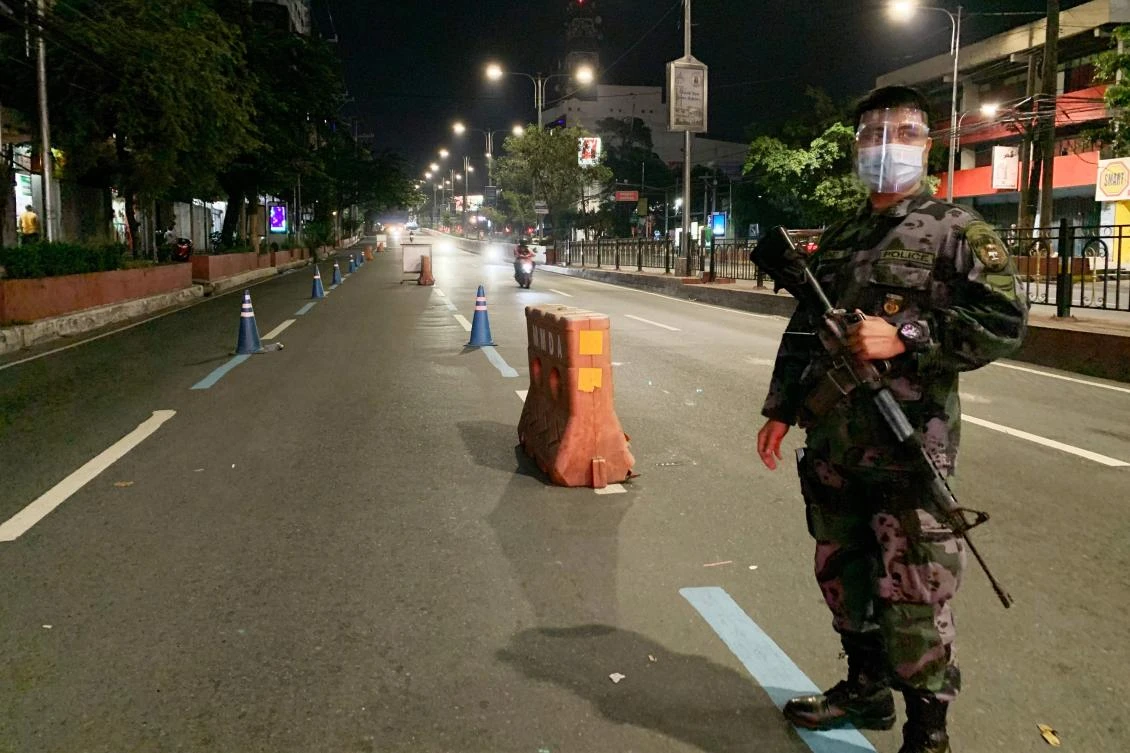 A policeman wearing a face mask and shield as a preventive measure against COVID-19, carries a rifle while standing guard at a check point in an almost empty road on the eve of Christmas, in Manila on December 24, 2020. (AFP)