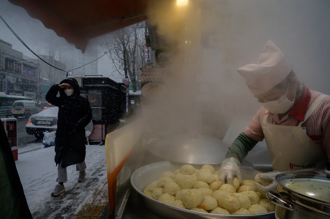 A vendor prepares dumplings at a stall at the entrance to a street market during a snow fall in Seoul on Jan. 12, 2021. (AFP)