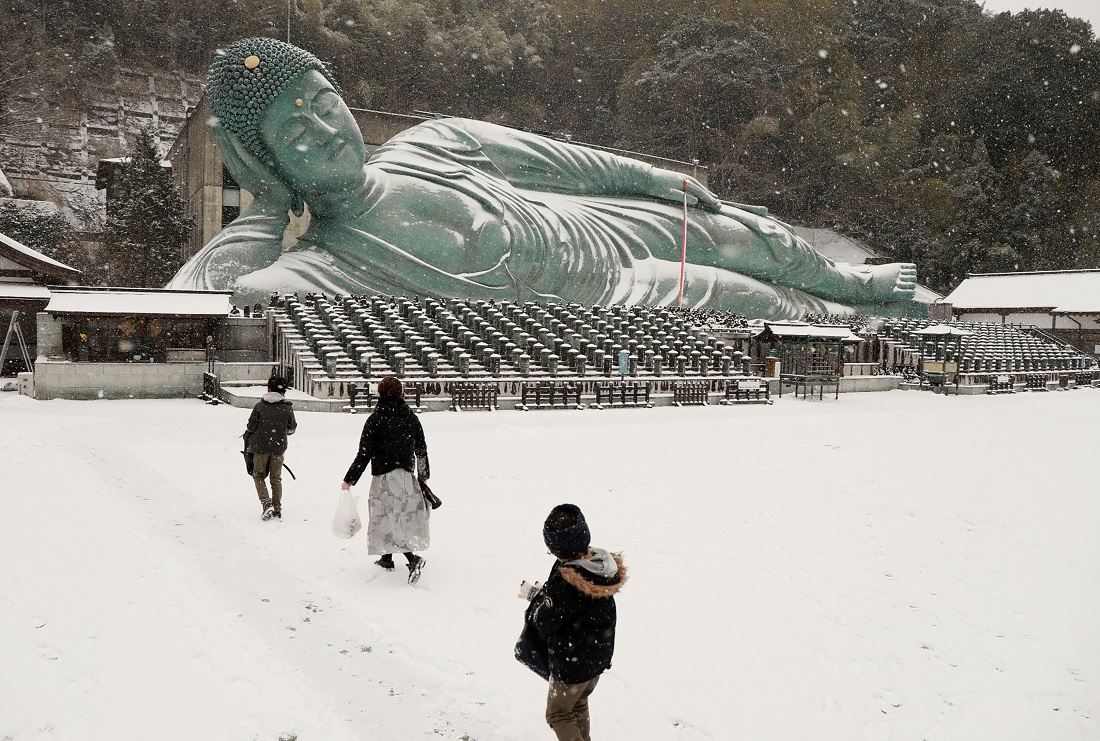 People walk on the snow-covered Nanzoin buddhist temple towards the bronze statue of reclining Buddha in Sasaguri town, Japan, Fukuoka prefecture on Jan. 8, 2021. (AFP)