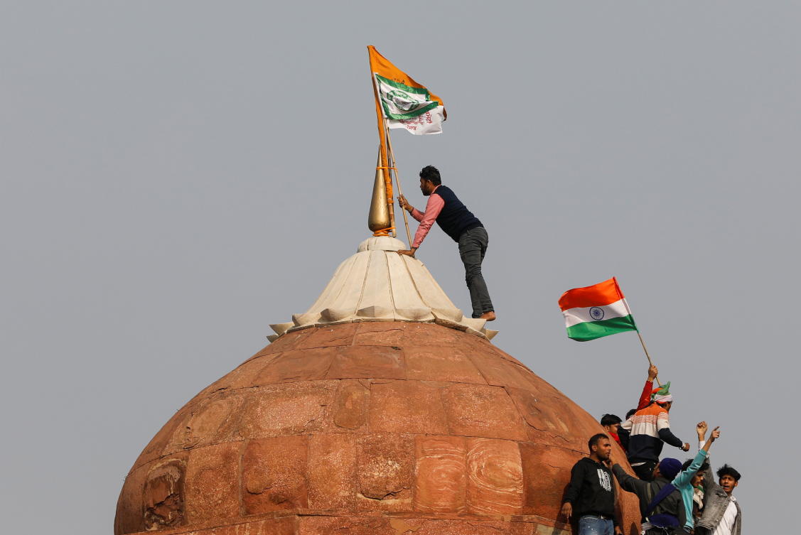 A farmer puts a flag on top of the historic Red Fort, during a protest against farm laws introduced by the government, in Delhi, India, January 26, 2021. REUTERS/Adnan Abidi