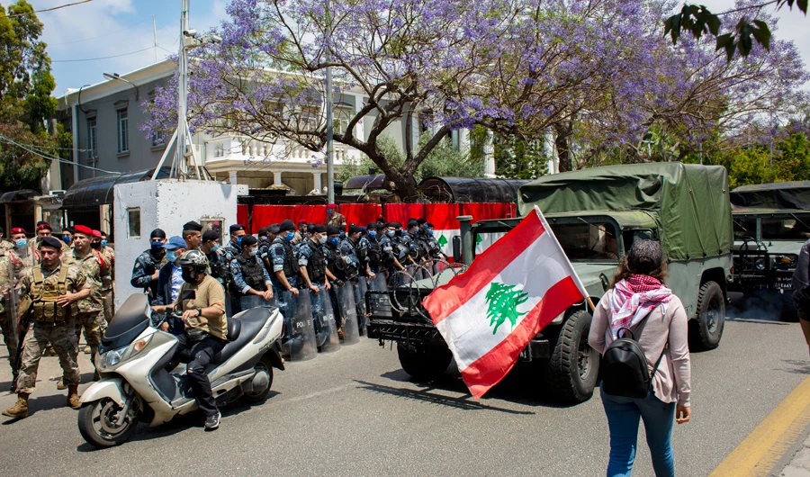 In this May 7, 2020 file photo, an anti-government protester walks by security forces holding a Lebanese flag during ongoing protests, outside the military court in Beirut, Lebanon. (AP)