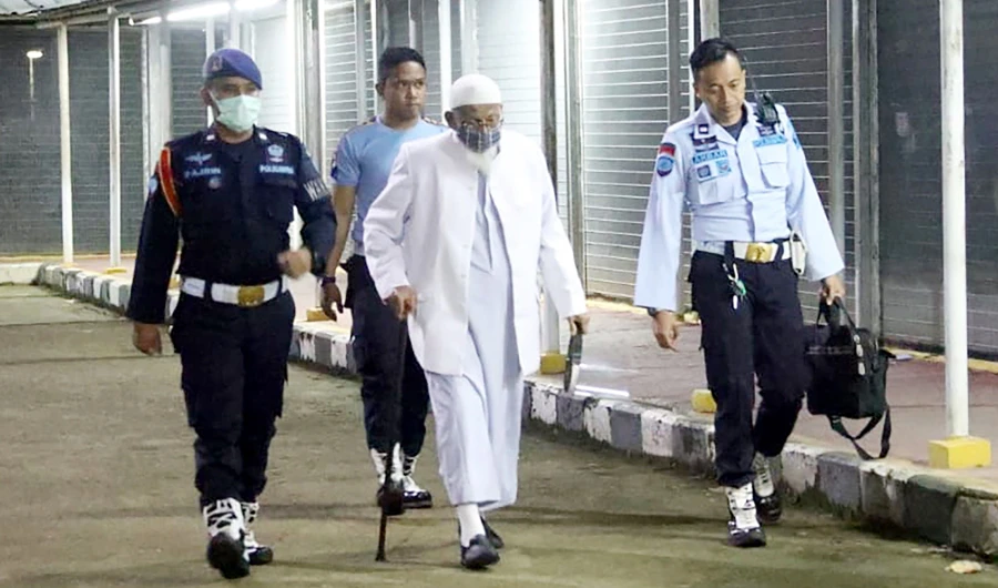This handout photo taken on January 8, 2021 and released by Indonesia National Prison shows Abu Bakar Bashir, 82 (C) being escorted by prison guards as he leaves the Gunung Sindur prison in Bogor, on the outskirts of Jakarta, after completing a 15 year prison term. (AFP)