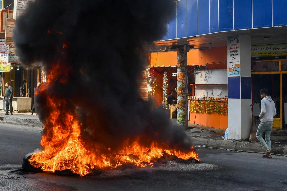 An Iraqi man walks next to burning tyres during clashes with police during anti-government demonstrations in the city of Nasiriyah in the Dhi Qar province in southern Iraq on January 10, 2021. (AFP)