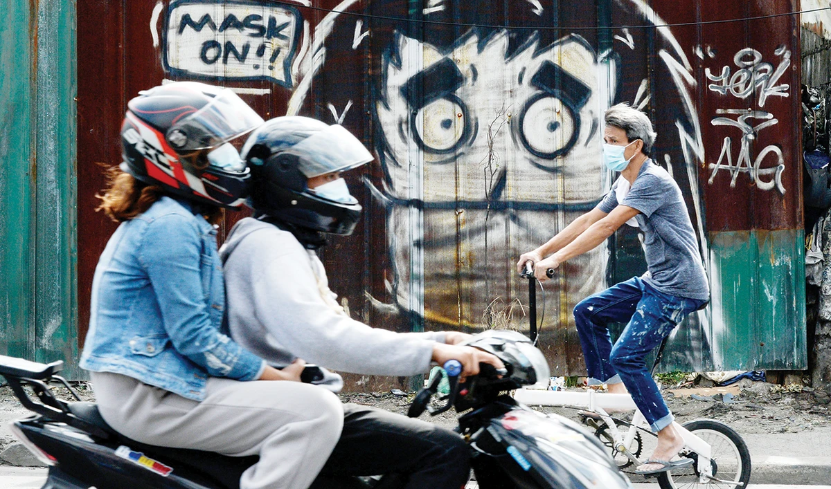 People wearing face masks as protection against COVID-19 pass by a mural reminding people to wear masks in Metro Manila on Monday. (Reuters)
