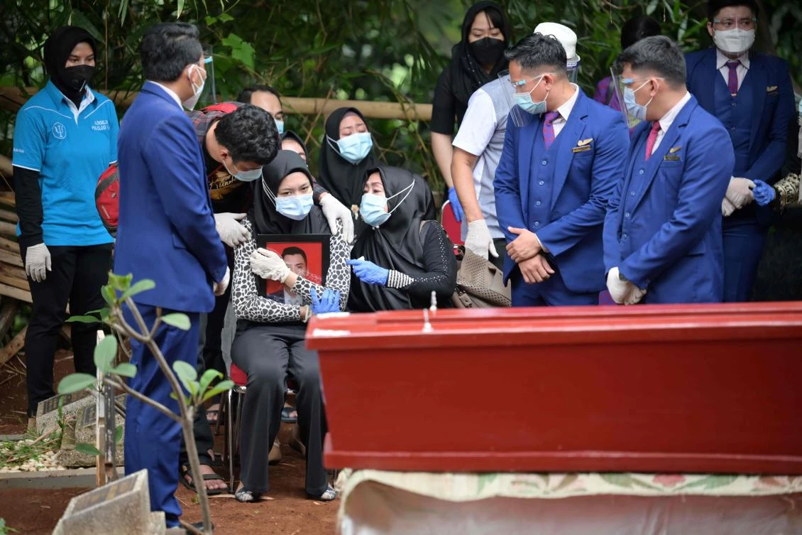Aldha Refa, the wife of Okky Bisma, a flight attendant and one of the 62 people aboard the ill-fated Sriwijaya Air flight SJ182, holds his photo while surrounded by family and friends during his funeral in Jakarta on Jan. 14, 2021. (AFP)
