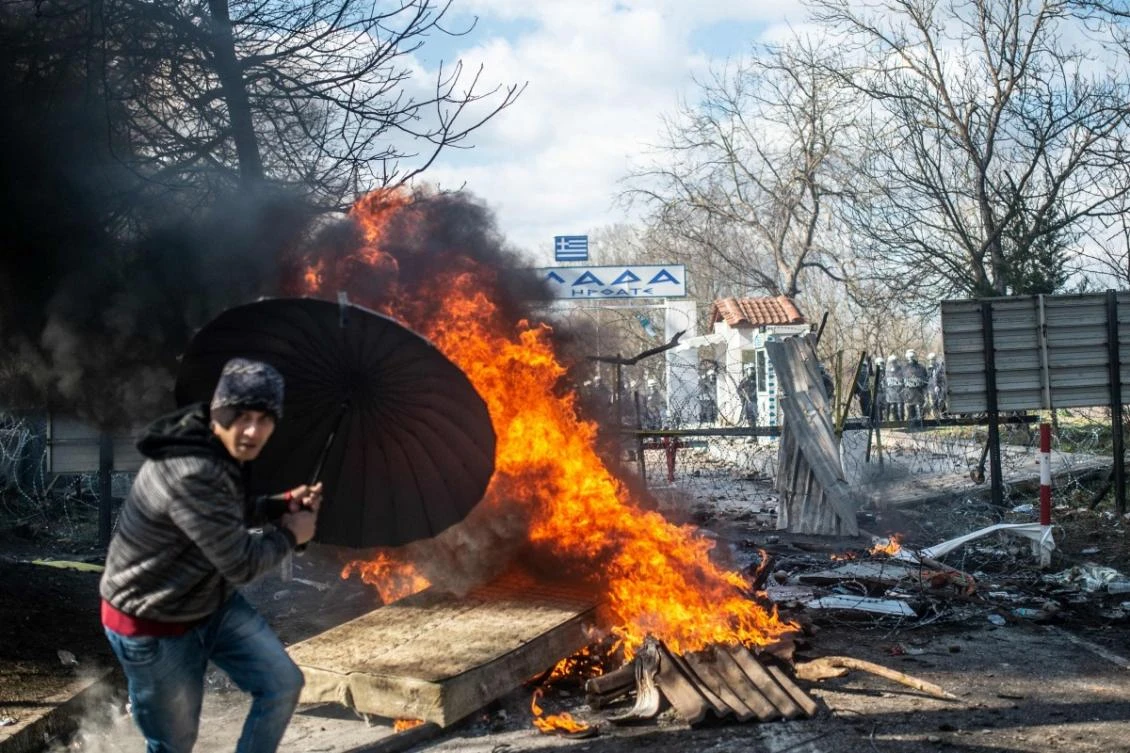 A migrant takes cover behind an umbrella during clashes with Greek police in the buffer zone on the Turkish-Greek border at Pazarkule. (AFP)