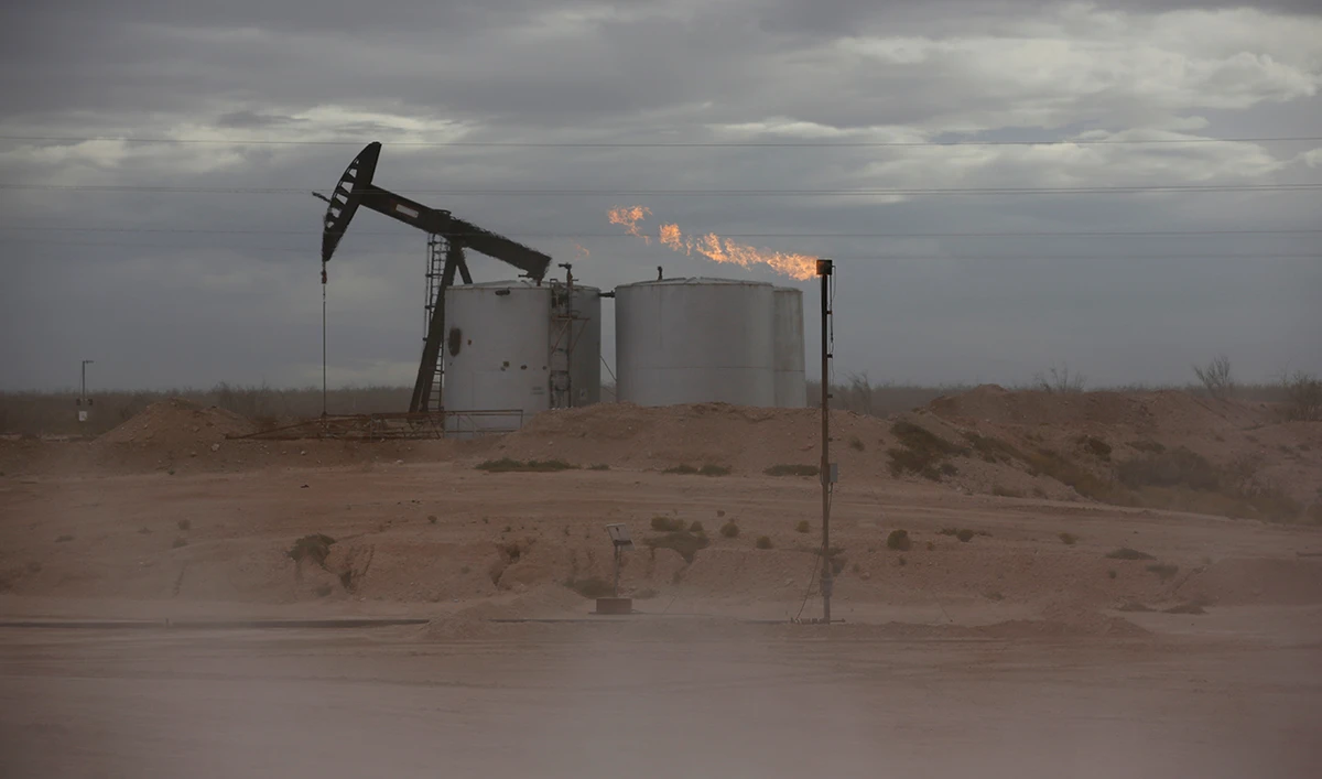 Dust blows around a crude oil pump jack and flare burning excess gas at a drill pad in the Permian Basin in Loving County, Texas, US. (Reuters/File)