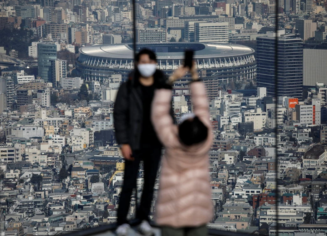 Visitors wearing protective face masks take photos with the National Stadium, the main stadium of Tokyo 2020 Olympics and Paralympics as the background. (Reuters)