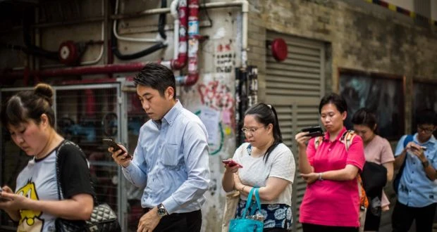 Commuters look at their mobile phones as they wait in line for a bus after finishing work in Hong Kong. (AFP)