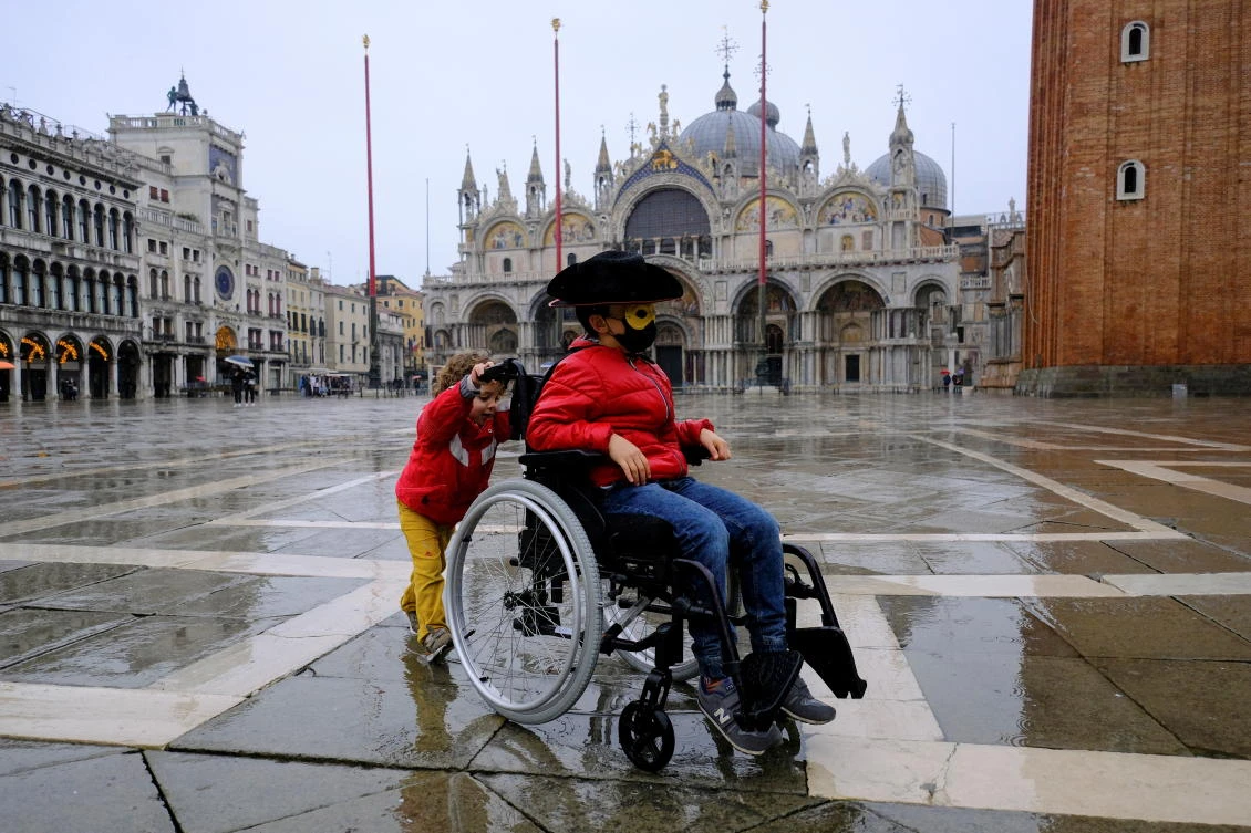 A child plays with their grandmother's wheelchair in St. Mark's square as people celebrate Venice's annual colourful carnival, which has been cancelled this year due to the coronavirus disease (COVID-19) pandemic, in Venice, Italy, February 7, 2021. REUTERS/Manuel Silvestri