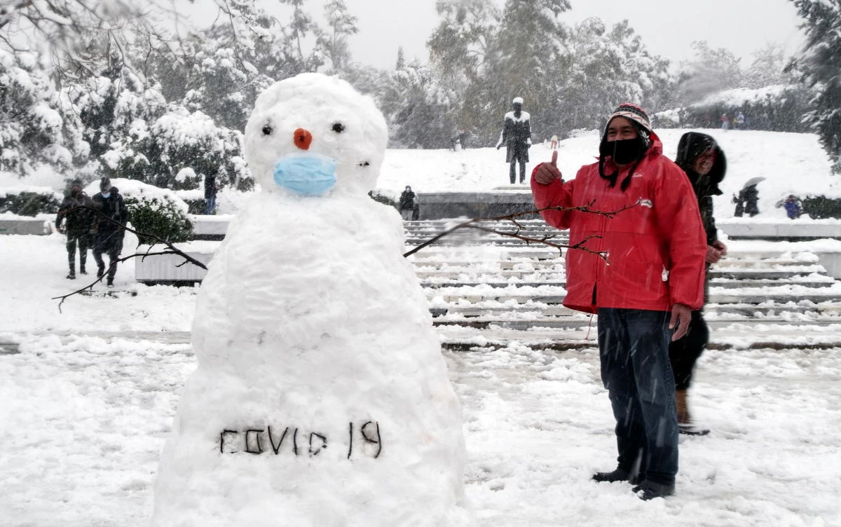 A man poses next to a snowman wearing a protective face mask and reading "COVID-19", in Athens, Greece, February 16, 2021. REUTERS/Vassilis Triandafyllou