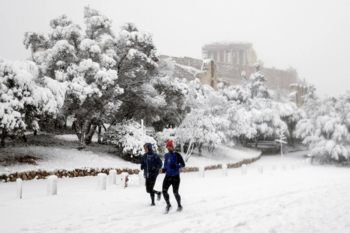 Two men jog as the Parthenon temple is seen atop the Acropolis hill archaeological site during a heavy snowfall in Athens, Greece, February 16, 2021. REUTERS/Alkis Konstantinidis TPX IMAGES OF THE DAY