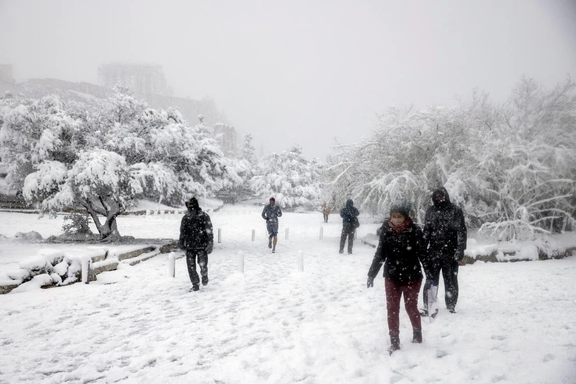 People make their way as the Parthenon temple is seen atop the Acropolis hill archaeological site during a heavy snowfall in Athens, Greece, February 16, 2021. REUTERS/Alkis Konstantinidis