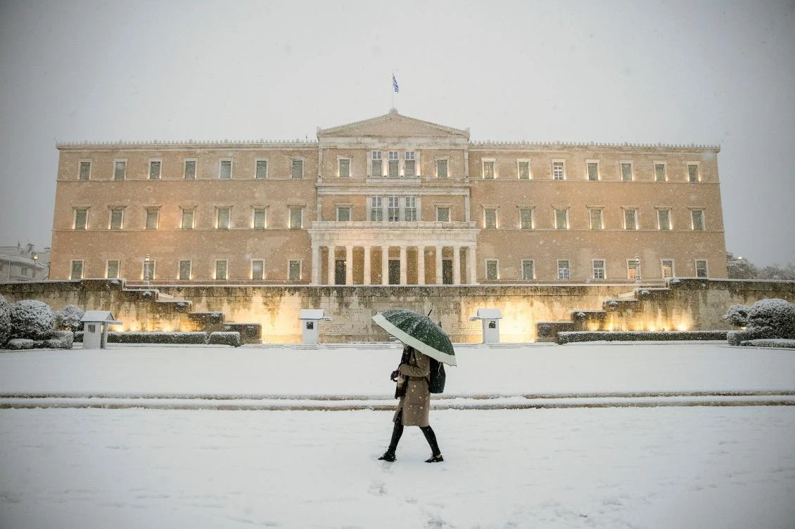 A woman holding an umbrella walks past the parliament building during heavy snowfall in Athens, Greece, February 16, 2021. REUTERS/Alkis Konstantinidis