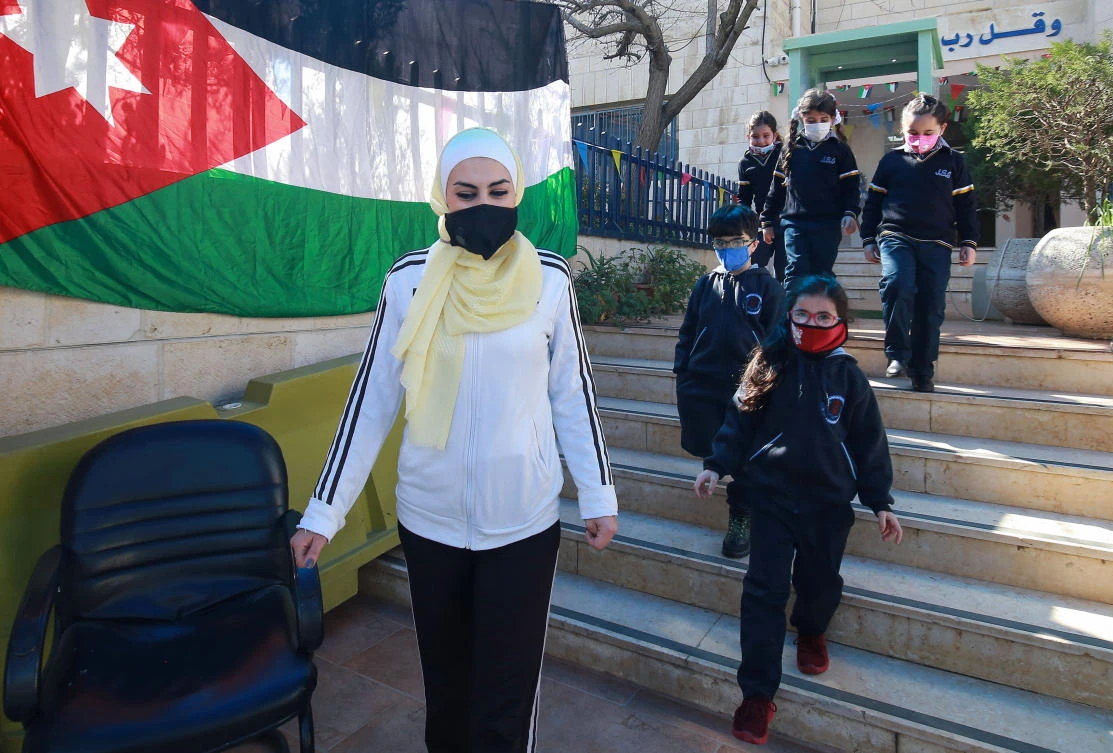 A Jordanian teacher accompanies pupils leaving the school building after attending class for the first time in nearly a year, in the capital Amman, on February 7, 2021. (AFP)