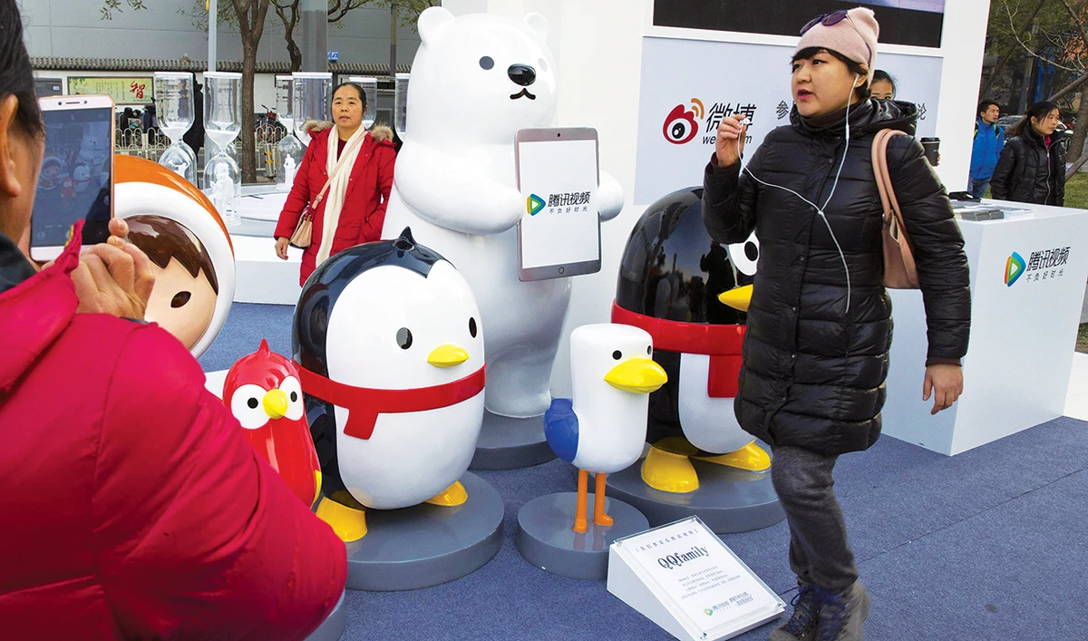 A woman wears her earphones as she walks past mascots representing the various platforms owned by Tencent Holdings Ltd. in Beijing. (AP/File)