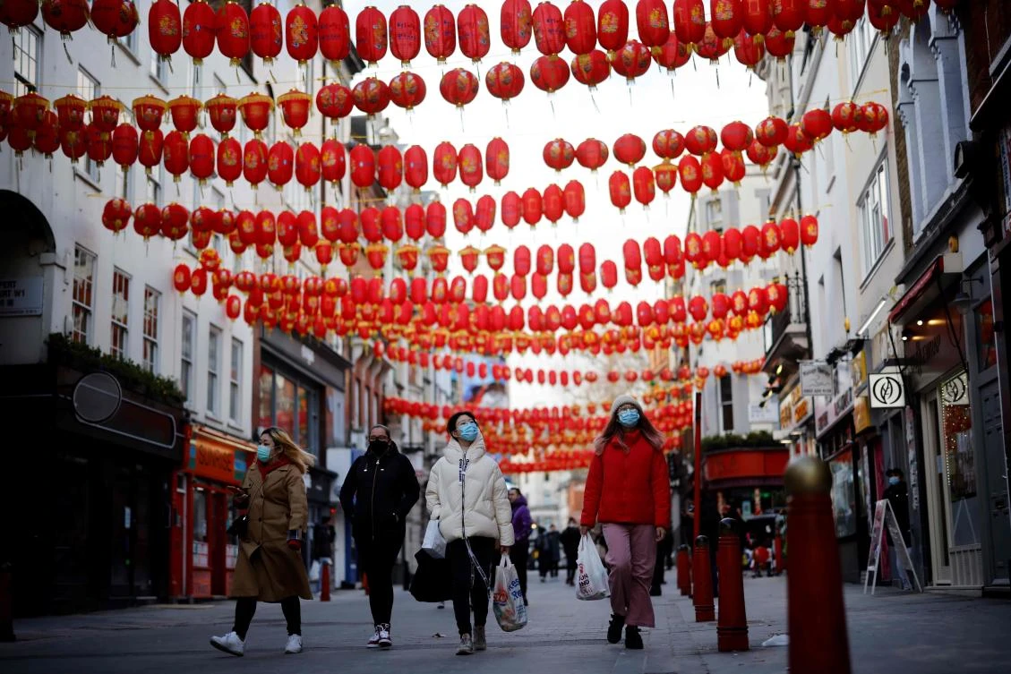 Pedestrians wearing facemasks walk along a street decorated with lanterns on the first day of the Lunar New Year, which ushers in the Year of the Ox in Chinatown, central London, Feb. 12, 2021. (AFP)