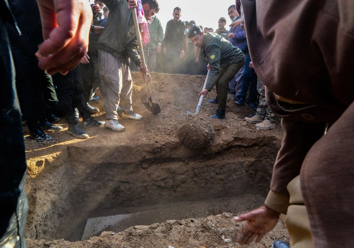Mourners gather around as a coffin is buried a coffin during a mass funeral for Yazidi victims of the Daesh group in the northern Iraqi village of Kojo in Sinjar district, on February 6, 2021. (Photo by Zaid Al-Obeidi / AFP)
