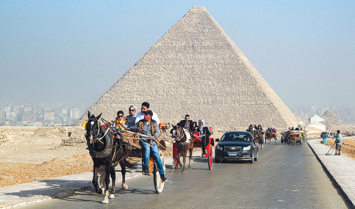 Tourists ride in the back of a horse-drawn cart near the Giza Pyramids Necropolis on the western outskirts of the Egyptian capital’s twin city of Giza. (File/AFP)