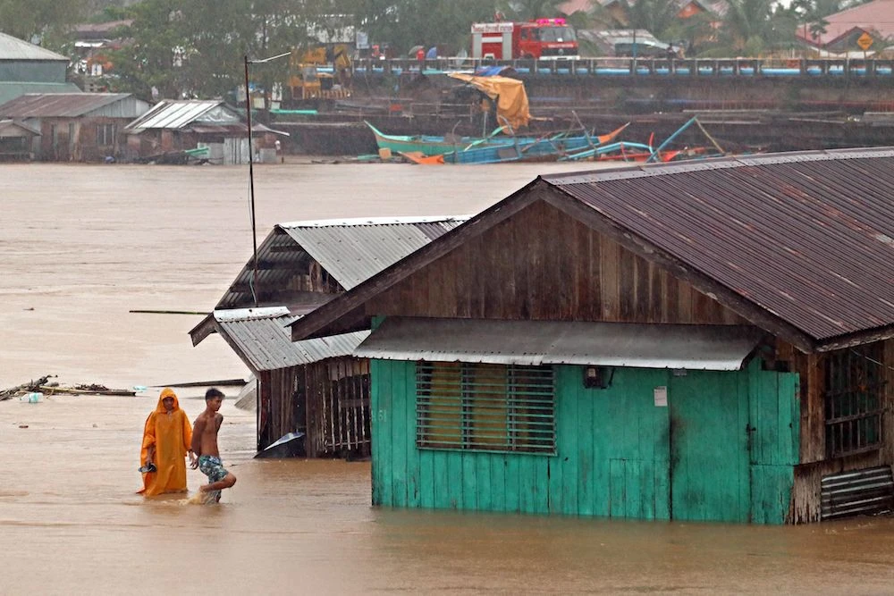 Residents walk past flooded houses near a swolen river due to heavy rain brought by Tropical Storm Dujuan in Tandag City, Surigao del Sur province, on Mindanao island, February 21, 2021. (AFP)