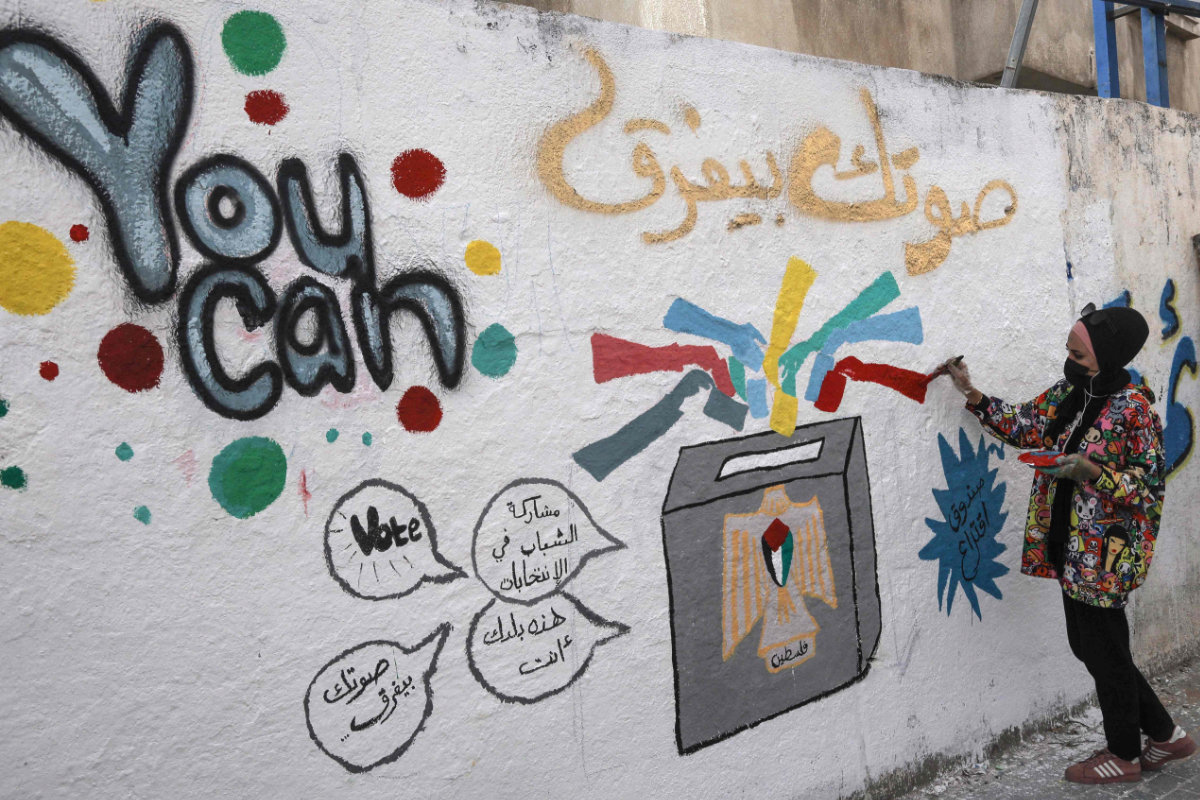 A Palestinian artist adds the final touches to a mural painting in a street in Gaza City on March 24, 2021, calling on people to vote during the upcoming elections. (AFP / MOHAMMED ABED)