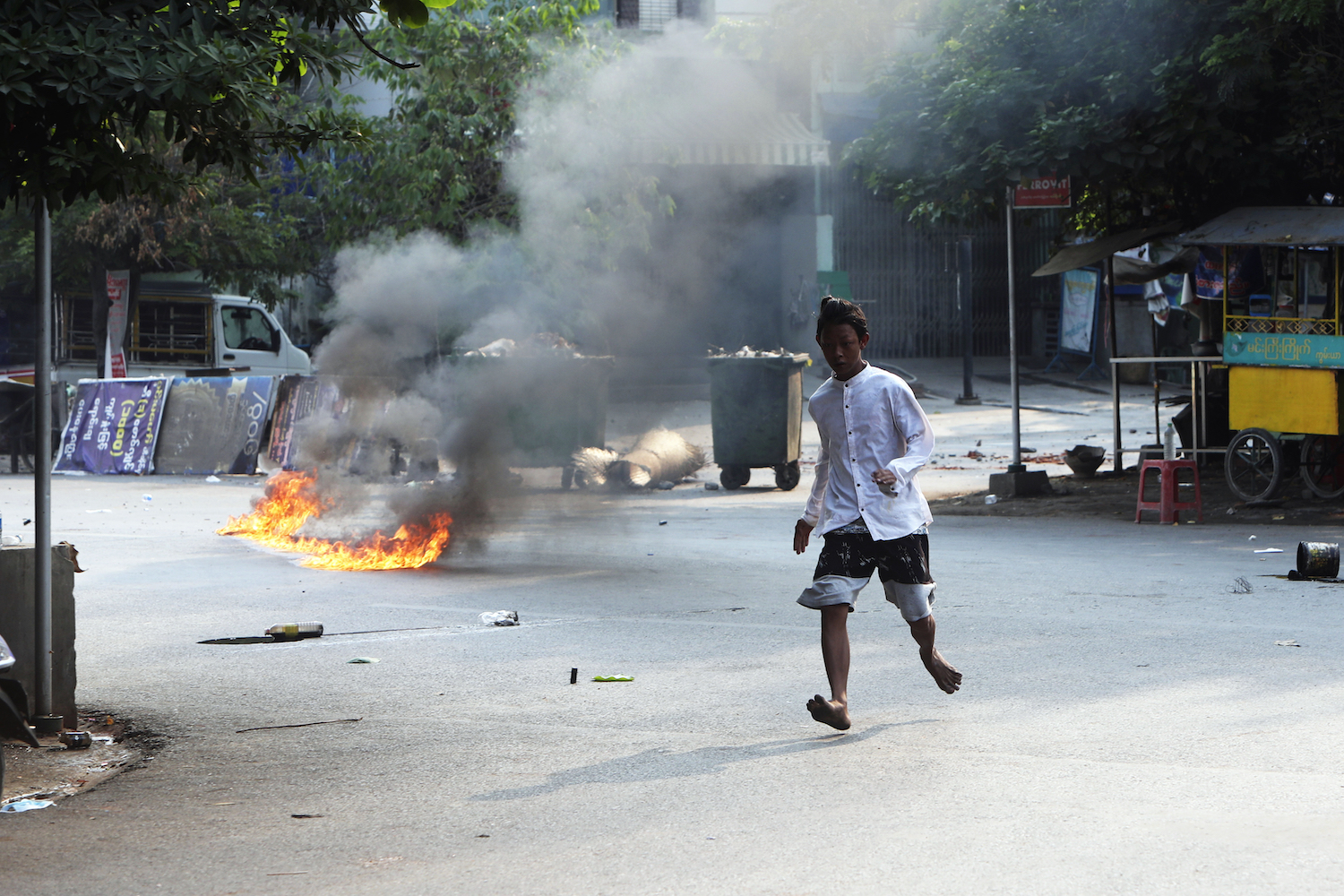 A man crosses the street while fire is seen in front of a road barricade that prevents security forces from advancing in Mandalay, Myanmar on March 14, 2021. (AP)