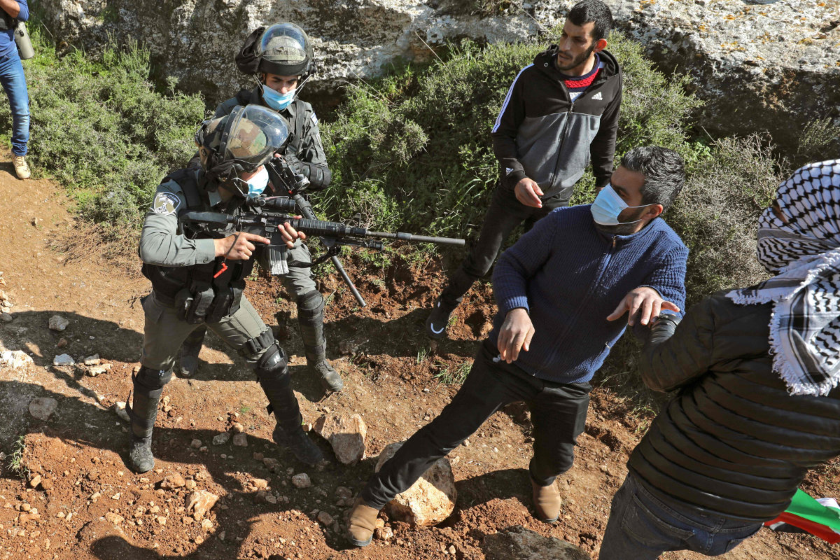 An Israeli soldier points his gun towards a Palestinian protester during a demonstration against Jewish settlements in the village of Beit Dajan in the occupied northern West Bank on March 5, 2021. (AFP / ABBAS MOMANI)