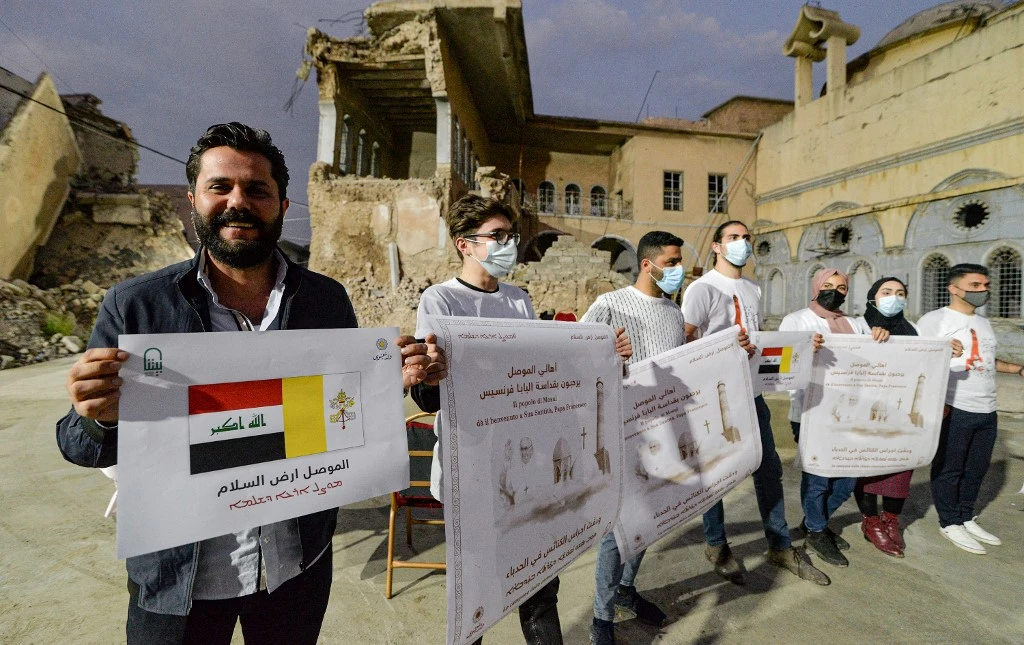 Volunteers stand holding posters welcoming Pope Francis in the ruins of the Syriac Catholic Church of the Immaculate Conception (Al-Tahira) in Mosul on March 2, 2021. (AFP)