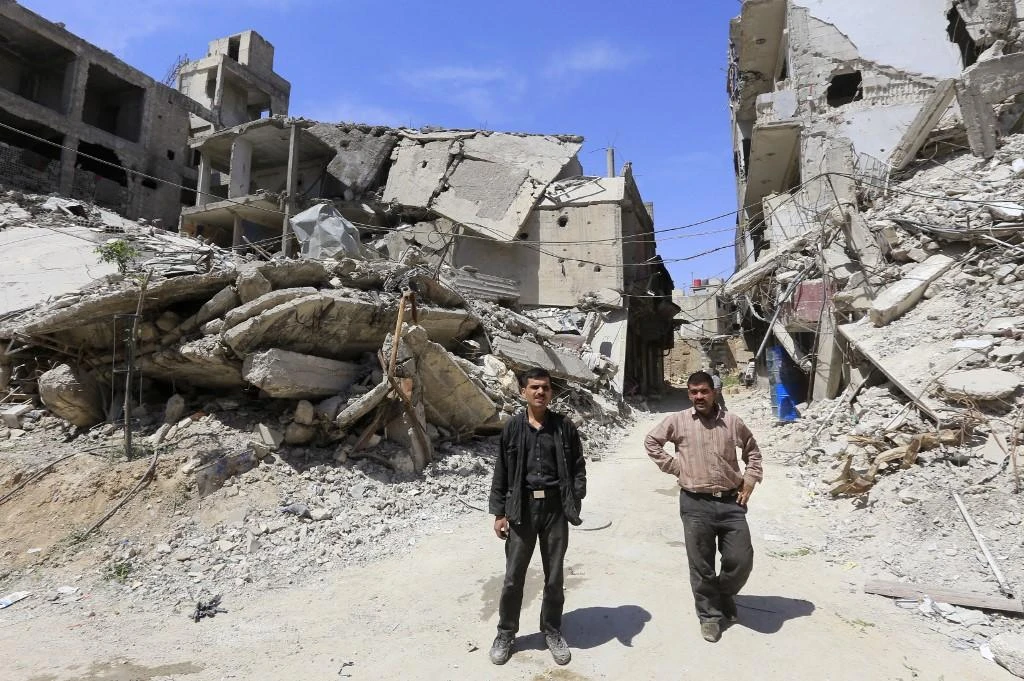 Syrians stand amidst destroyed buildings in Douma on the outskirts of Damascus on April 16, 2018 during an organized media tour. (File/AFP)
