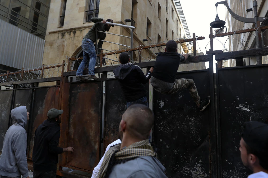 Anti-government protesters climb a metal wall installed by security forces to prevent protesters from reaching the Parliament building, during a protest in Beirut, Lebanon, Saturday, March. 13, 2021. (AP)