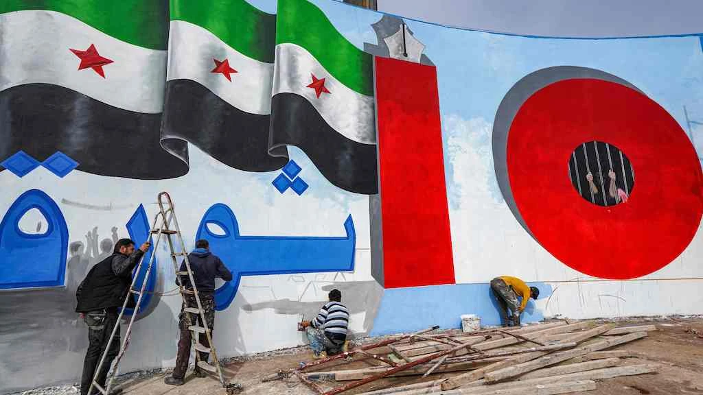 Activists paint the wall of a landmark erected in a roundabout in Idlib on March 14, 2021, a day ahead of the 10th anniversary of the uprising against Bashar al-Assad. (AFP)