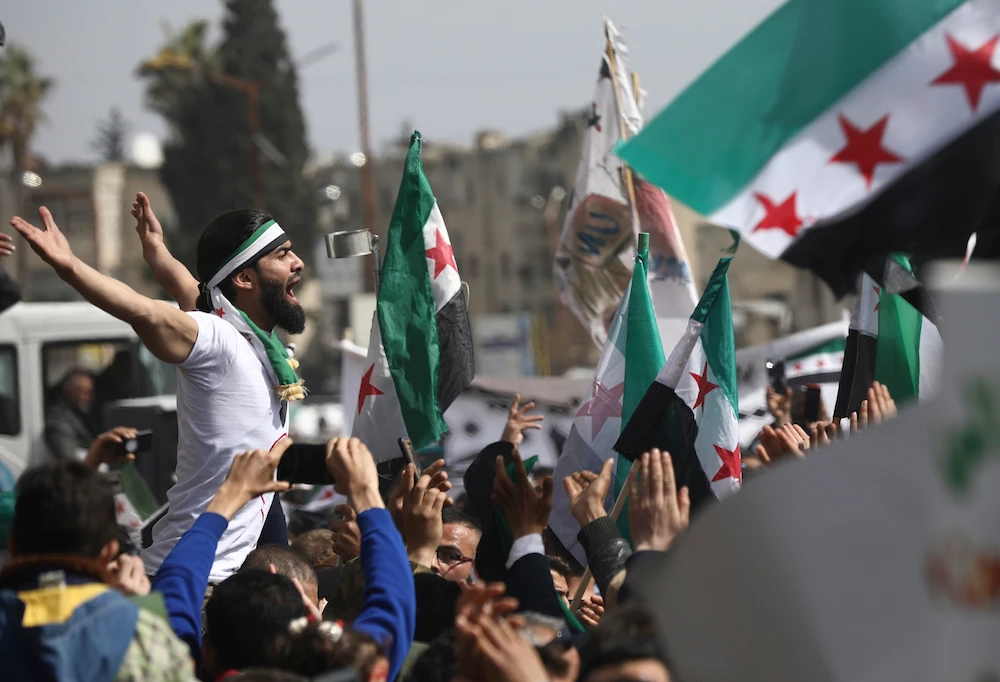 An anti-Syrian government protester shouts slogans as others wave revolutionary flags, to mark 10 years since the start of a popular uprising against President Bashar Assad’s rule, in Idlib, northwest Syria, Monday, Mar. 15, 2021. (AP)