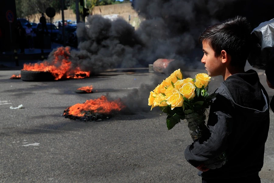 A Syrian boy who sells flowers on the street watches protesters burn tires during a protest against the increase in prices of consumer goods in Beirut, Lebanon. (AP)