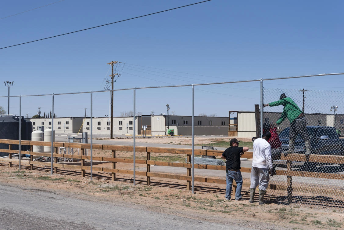 A crew works on constructing a tall chain link fence that will surround a facility for migrant children and teenagers from the southern border of the US on March 20, 2021 south of Midland, Texas. (Eli Hartman/Odessa American via AP)