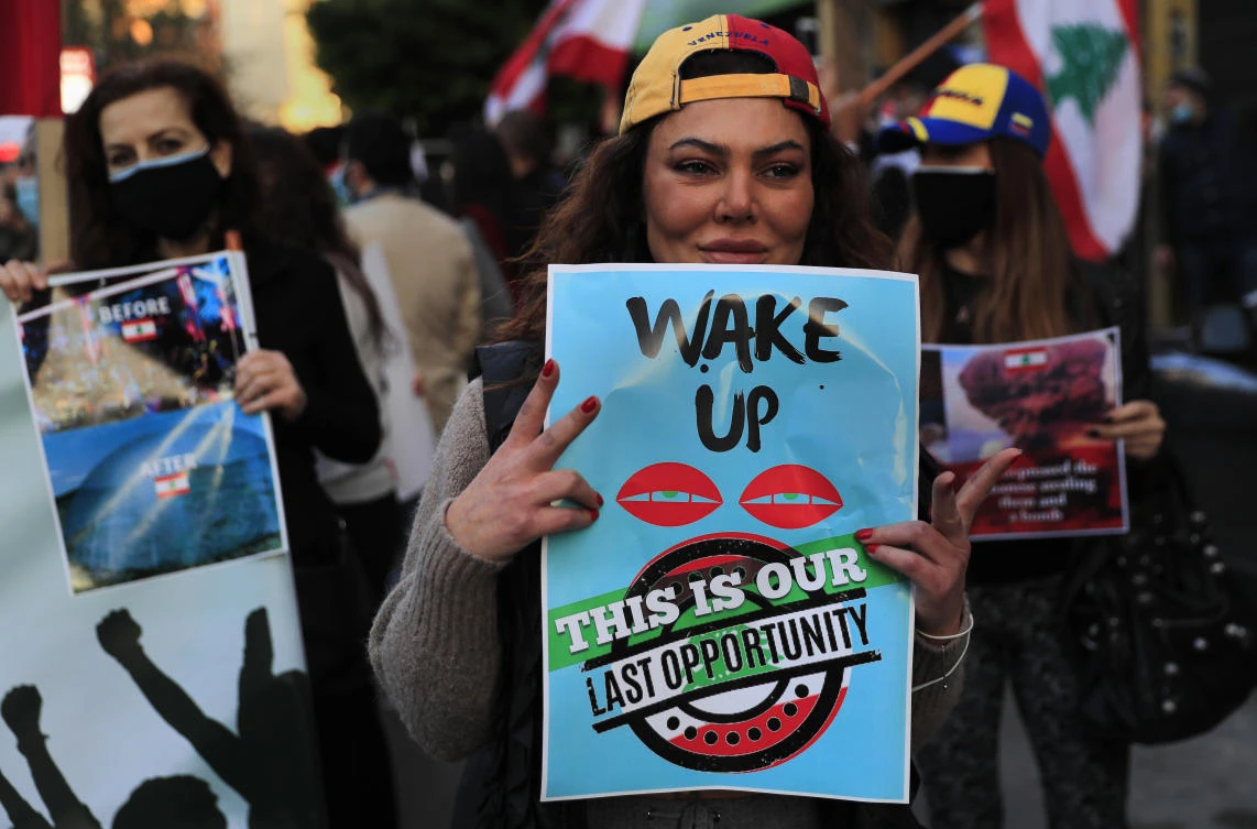 A protester flashes victory signs and holds placards, as she marches during a protest against the increase in prices of consumer goods and the crash of the local currency in Beirut, Lebanon, Friday, March 19, 2021. (AP Photo/Hussein Malla)