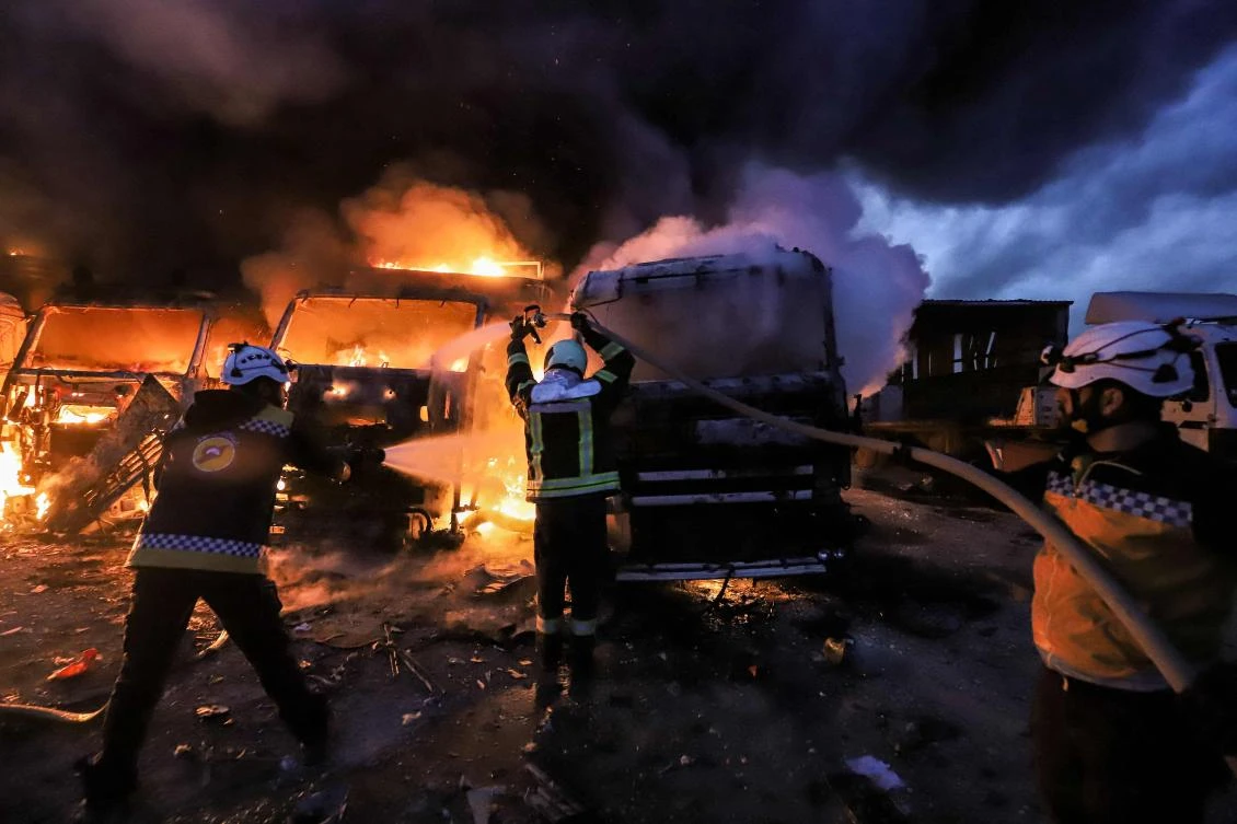 Members of the Syrian civil defence try to put out several trucks and freight vehicles on fire in the aftermath of air strikes at a depot near the Bab al-Hawa border crossing between Syria and Turkey in Syria's rebel-held northwestern Idlib province. (AFP)