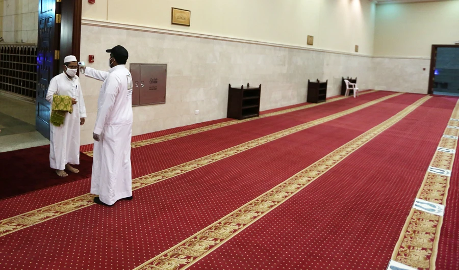 A volunteer checks the temperature of a man as he arrives to perform the dawn prayer at a mosque in the Saudi holy city of Makkah on June 21, 2020. (AFP)