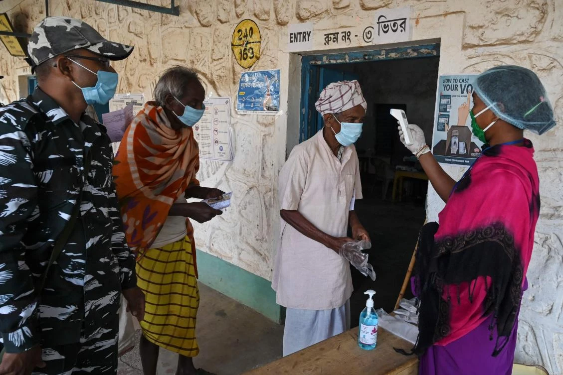 A volunteer checks a voter’s body temperature entering a polling station to cast his ballot in West Bengal’s legislative election on March 27, 2021. (AFP)