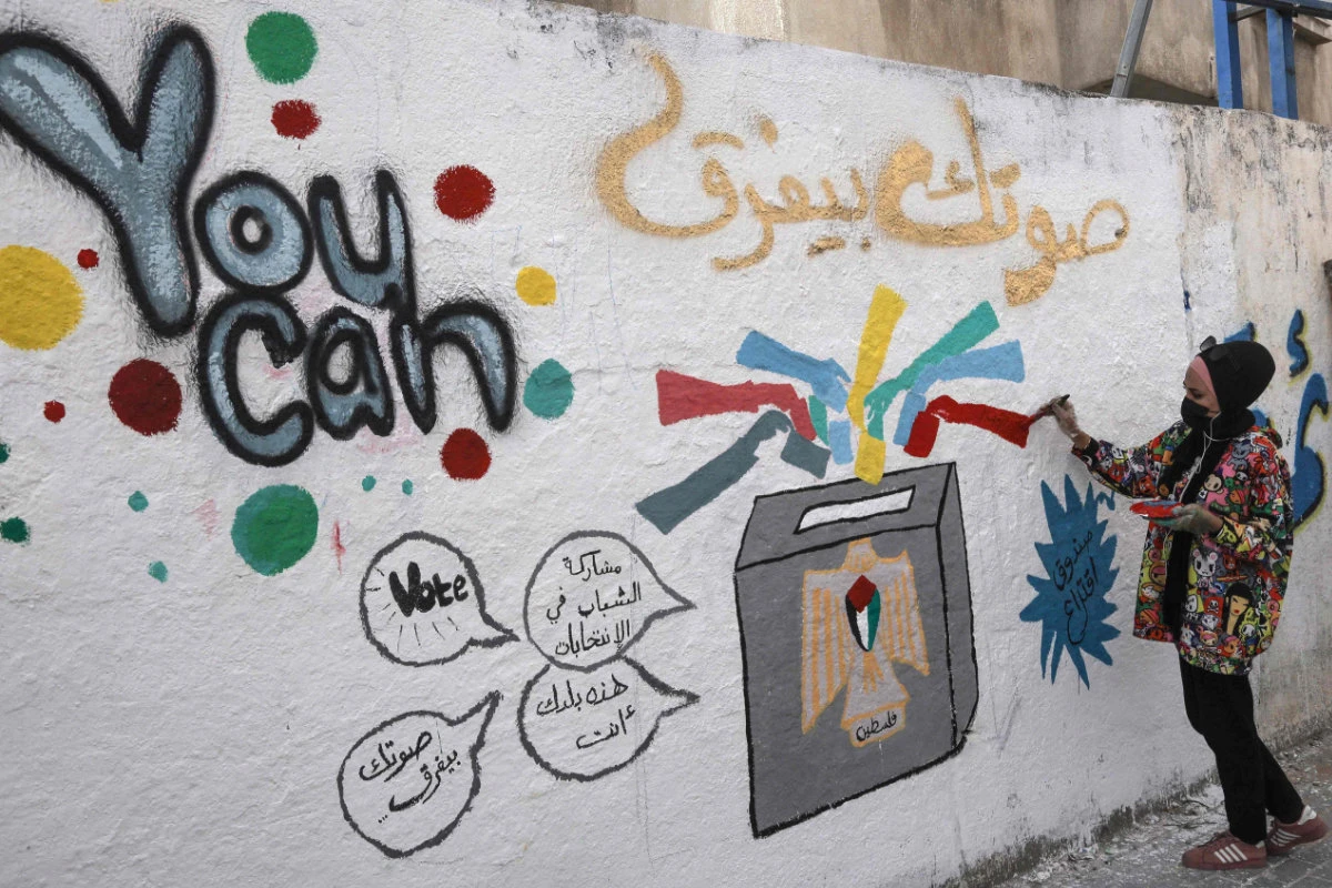 A Palestinian artist adds the final touches to a mural painting in a street in Gaza City on March 24, 2021, calling on people to vote during the upcoming elections. (AFP / MOHAMMED ABED)
