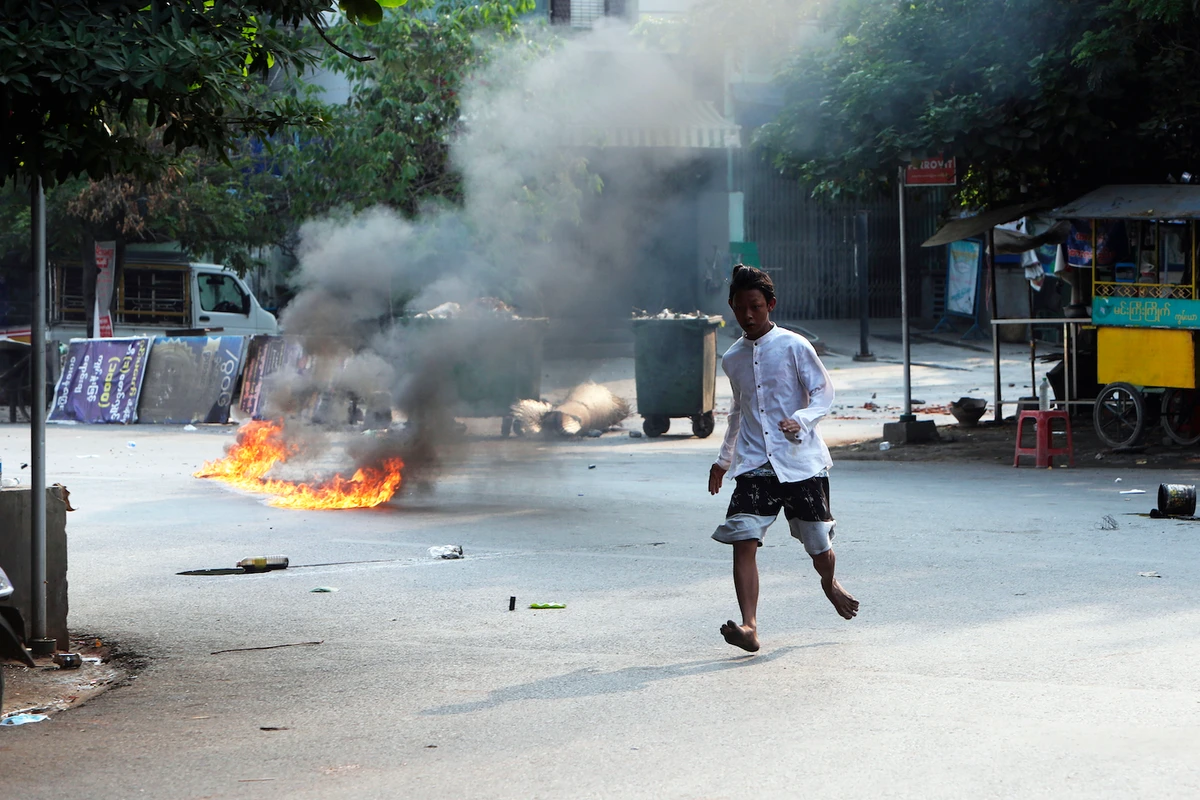 A man crosses the street while fire is seen in front of a road barricade that prevents security forces from advancing in Mandalay, Myanmar on March 14, 2021. (AP)