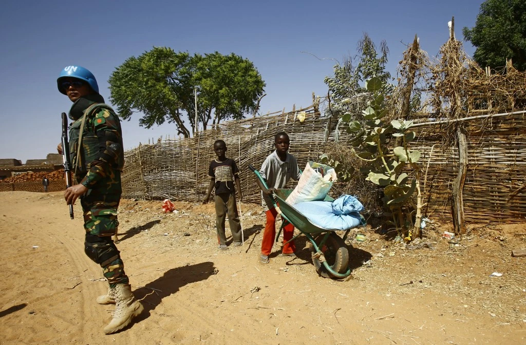 Sudanese boys push a wheelbarrow past a United Nations peace keeper at the El-Riyadh camp for internally displaced persons (IDP) in Geneina, the capital of the state of Sudan's West Darfur. (File/AFP)
