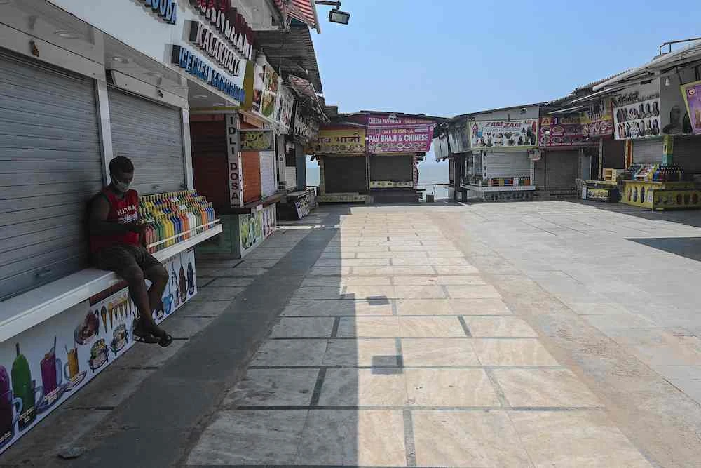 A man checks his mobile phone while sitting outside a closed shop, during restrictions imposed by state government, amidst rising Covid-19 infections, Mumbai, India, April 15, 2021. (AFP)