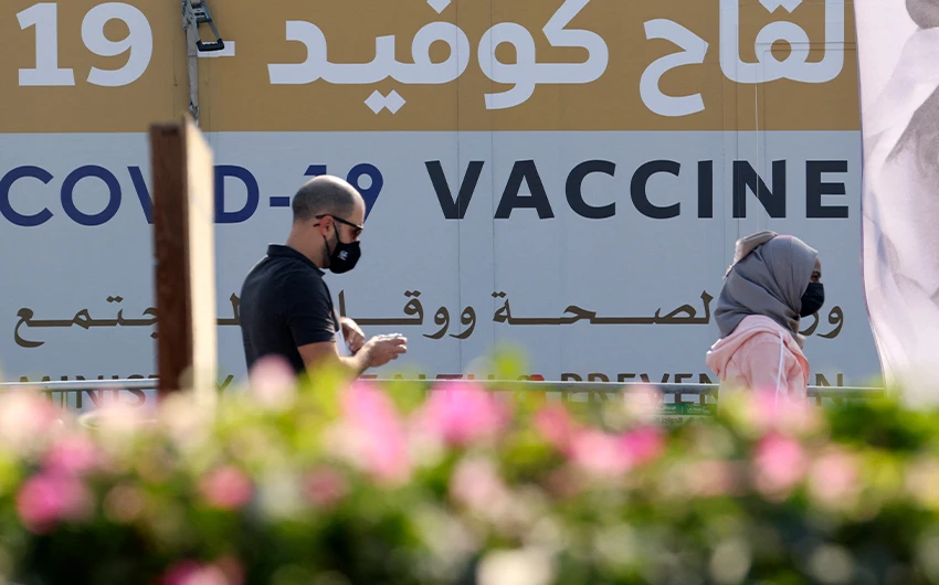 A man and a woman walk past a huge health ministry COVID-19 vaccines announcement outside a medical center in Dubai on February 16, 2021. (AFP/File)