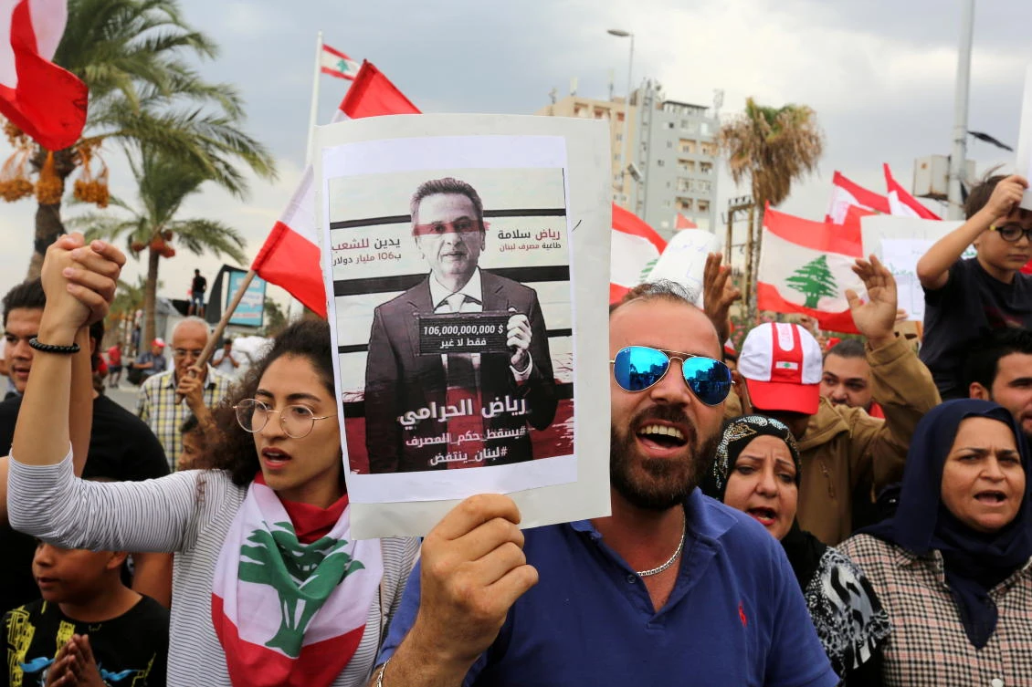 Lebanese demonstrators carry a banner depicting Lebanon's Central Bank Governor Riad Salameh, who along with his brother, are being probed over suspected embezzlement of $300 million based on a Swiss legal request. (REUTERS)