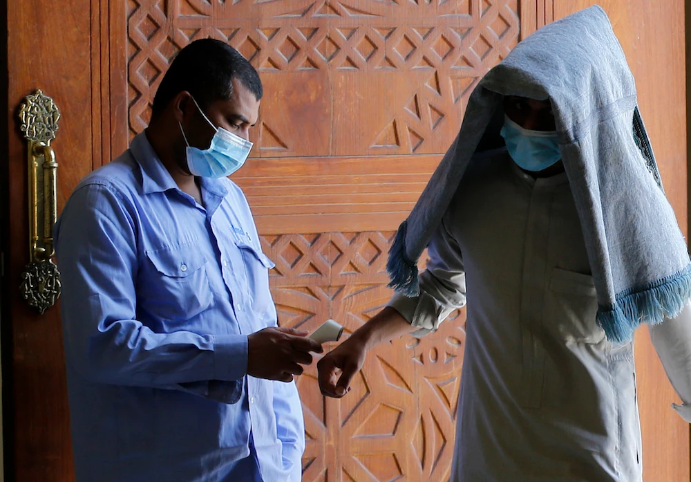 A worshipper covered by his prayer carpet and wearing a mask to curb the spread of the coronavirus has his temperature measured as he enters Al- Jaffali mosque, Jeddah. (AP)