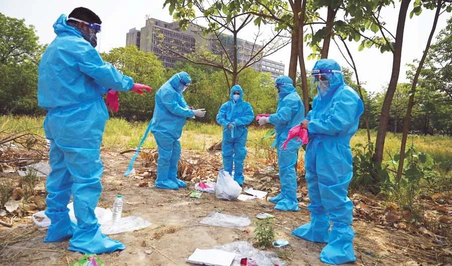 Relatives and friends put on personal protective equipment (PPE) suits on Friday before the burial of their loved one at a graveyard in New Delhi. (AFP)